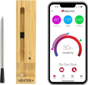 Wireless meat thermometer with bamboo charger and smartphone app displaying internal, target, and ambient temperatures.