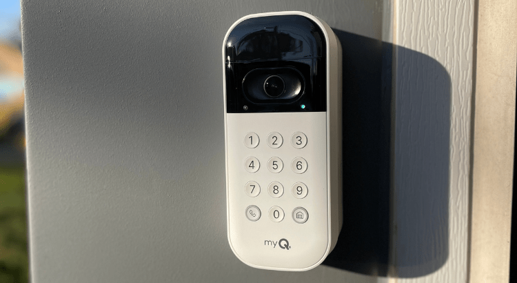 A myQ smart garage door keypad with a camera and numeric buttons, mounted on an exterior wall.