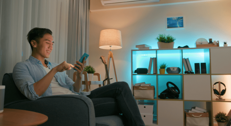 Student sitting in a modern, well-lit living dorm room using a smartphone to control smart home devices, showcasing the convenience of smart home technology.