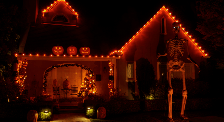 Halloween-decorated house glowing with orange lights and giant skeleton.